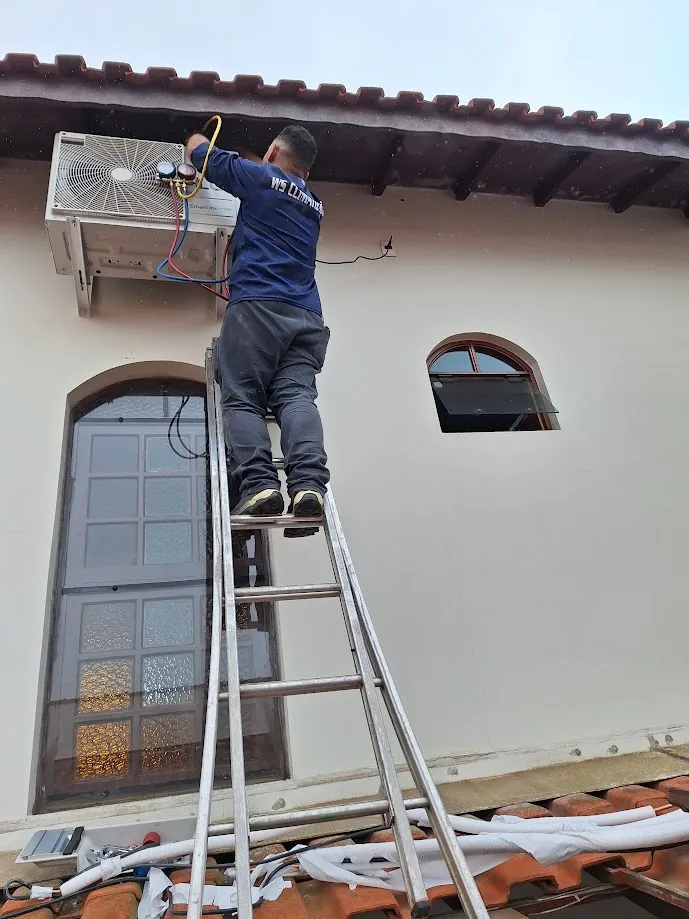 Técnico da WS instalando condensadora em fachada de residência com escada